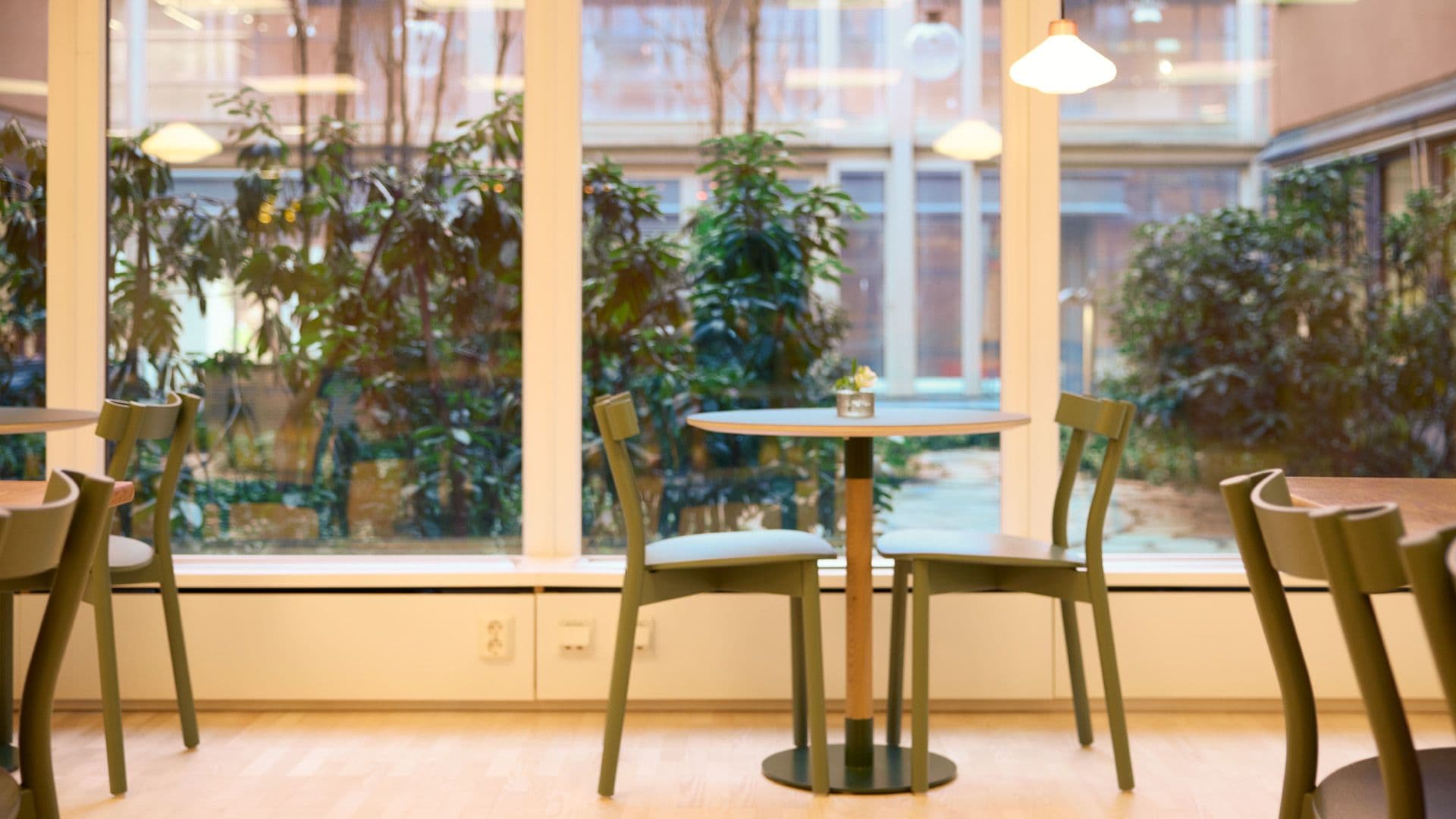 Modern reception med gröna stolar och runda bord, stora fönster ut mot grön innergård.