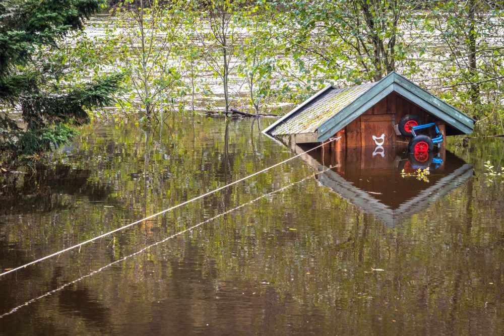 Liten stuga som flyter i vattnet under en översvämning, bunden med ett rep {:}{:en}Small cabin floating in the water during a flooding, tied with a rope{:}
