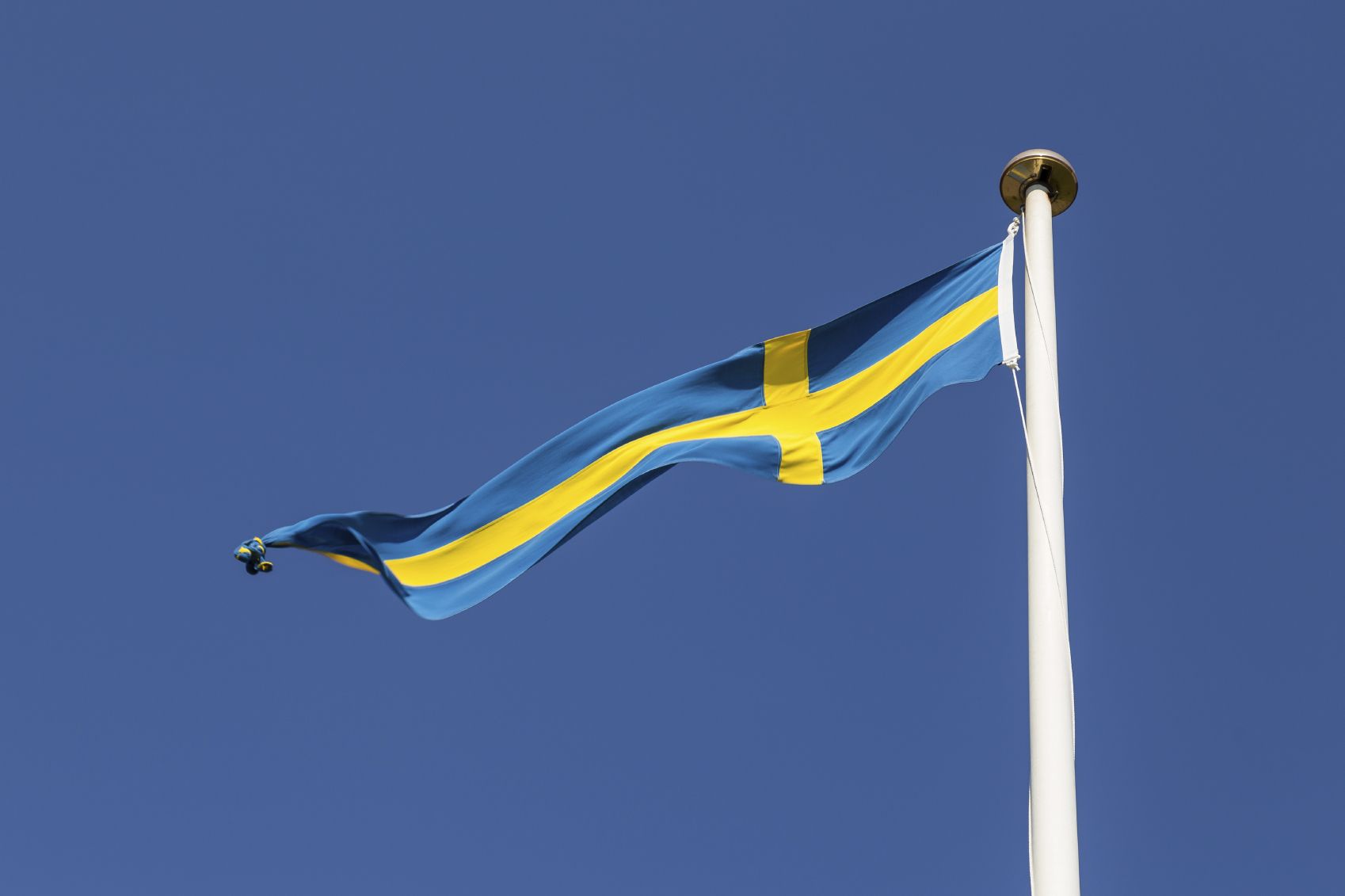 Svenska flaggan i flaggstång mot blå himmel{:}{:en}Flagpole with Swedish flag against a blue sky{:}