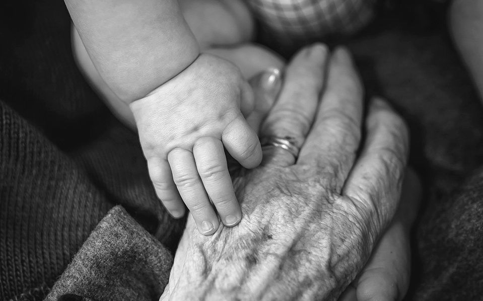 En äldre persons hand möter en bebishand